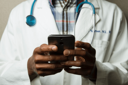 Médico com estetoscópio ao redor do pescoço digitando no celular